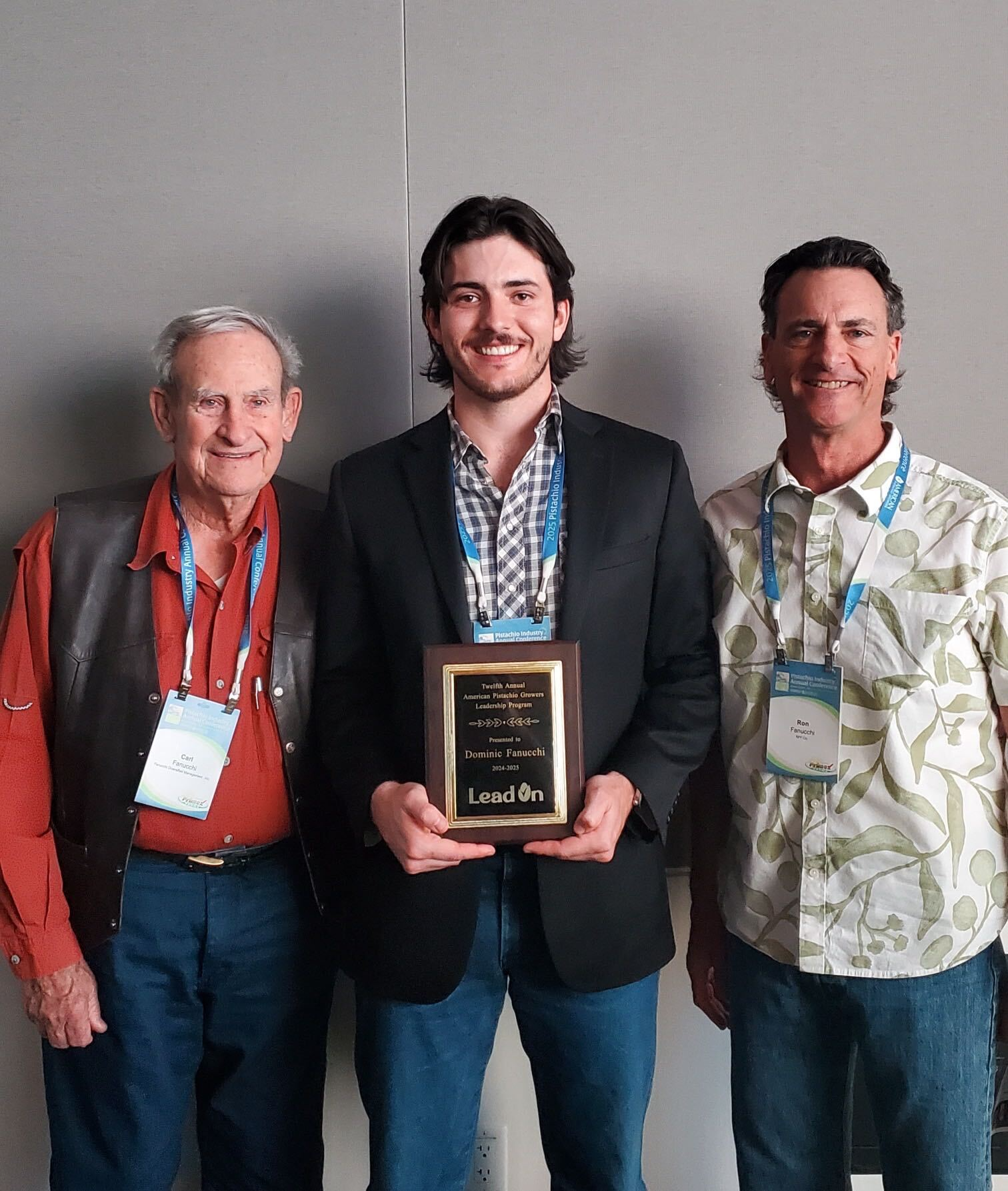 Dominic Fanucchi at the APG LeadOn graduation holding his graduation plaque with his grandpa and uncle beside him
