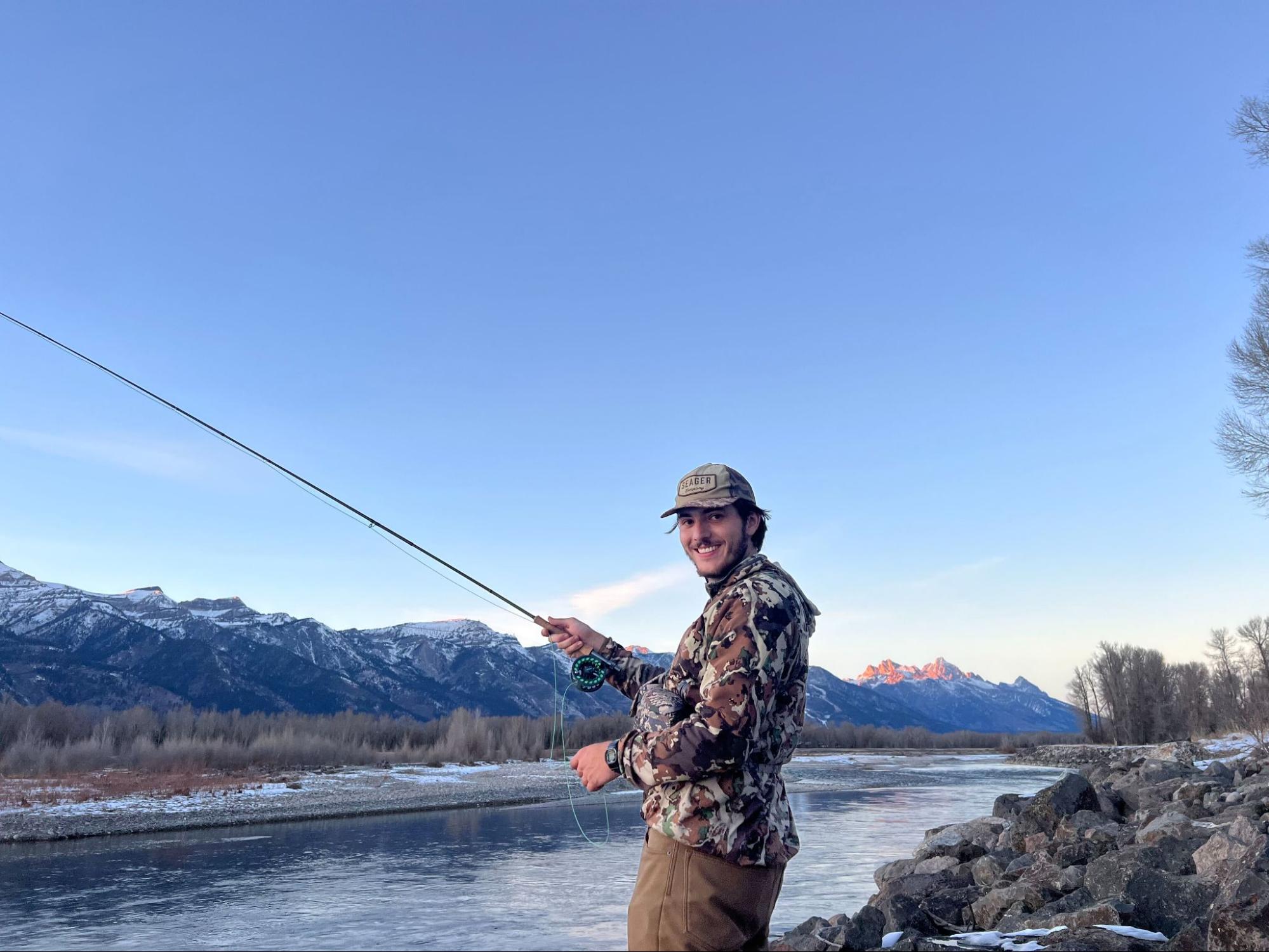 Dominic fly fishing on a river with snowcapped mountains in the background